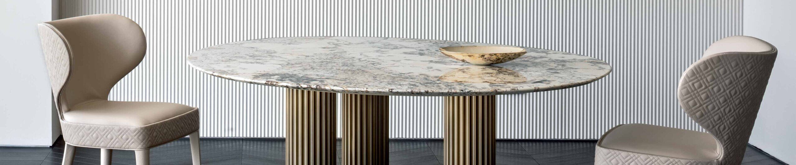 Round marble dining table with fluted metal base and two upholstered chairs