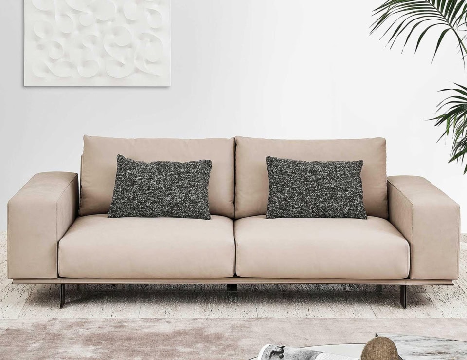 Beige leather sofa with two dark fabric cushions in a living room setting